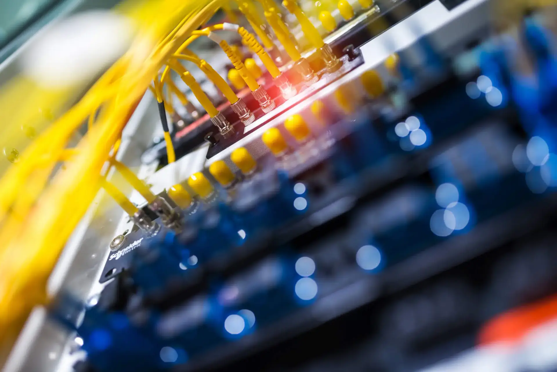 Iron Fibre Networks Yellow network cables plugged into ports on a server with indicator lights, accompanied by a red LED glowing in the center of the image—illustrating the importance of robust Fibre Optic Cable Solutions & Services in modern data infrastructure. Fibre Optic Cable Solutions & Services